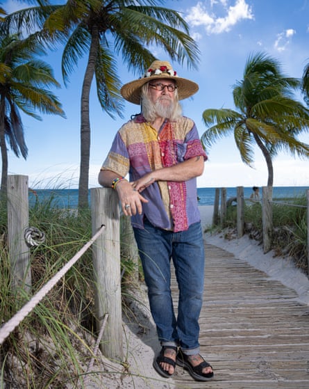 Billy Connolly standing on a quay, surrounded by palm trees with the sea behind him