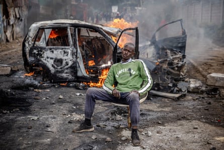 An opposition supporter sits in front of a car set on fire by protesters during riots in Nairobi