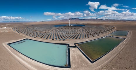 A solar tower surrounded by curved arrays of mirrors in a Nevada desert, with water reservoirs in the foreground
