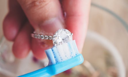 A close-up of a hand holding a diamond ring and cleaning it with a toothbrush and bubbles