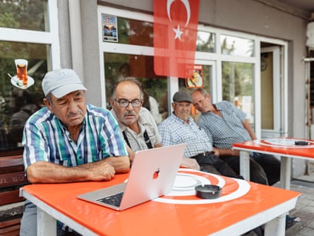 Özenç and friends look at a laptop outside a cafe.
