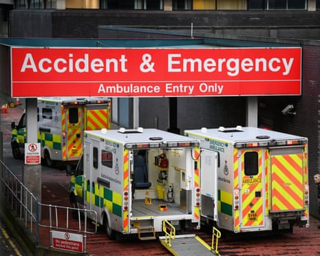 Multiple ambulances parked outside a hospital accident and emergency entrance beneath a large red sign.