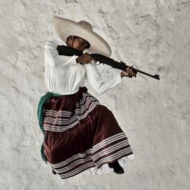 A woman wearing a wide brimmed hat jumping in the air and pointing a rifle gun.