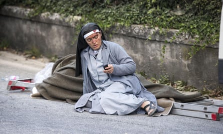 A nun checks her mobile phone as she lies near an earthquake victim in Amatrice.