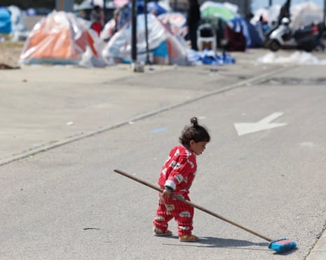 A child holds a broom next to displaced people's tents in Beirut.