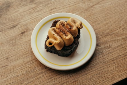 A dark cake square topped with swirled, piped cream and chocolate shavings sits on a white plate