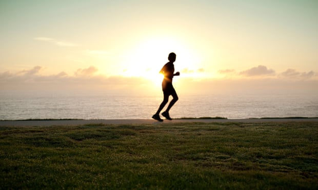 A silhouette of a jogger running alone with sun on horizon