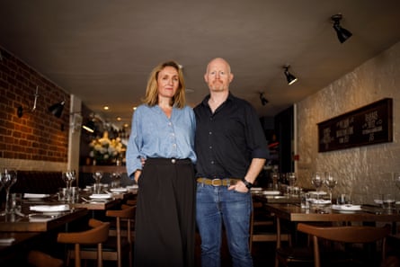 A man and a woman pose in a restaurant alongside empty tables.
