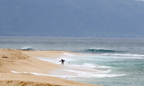 A surfer walks out of the ocean on Oahu’s north shore near Haleiwa. Encouraging people to stay away has severely damaged Hawaii’s economy, which relies heavily on the tourist dollar.