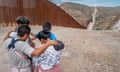 A group of migrants praying together near a wall at the US-Mexico border.