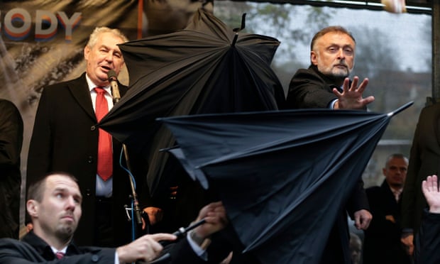 Security personnel use umbrellas to protect Miloš Zeman from missiles thrown by protesters during a speech in 2014