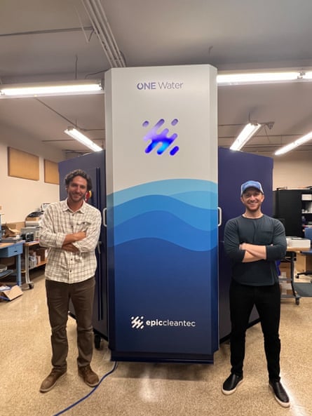 Two men stand next to water treatment equipment.