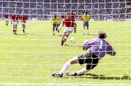 The England striker Gary Lineker takes a penalty which the Brazil goalkeeper Carlos, diving to his right, is about to save easily.
