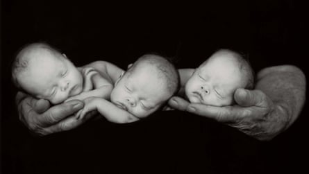 The black and white image shows the three tiny infans side by side in a man’s hands