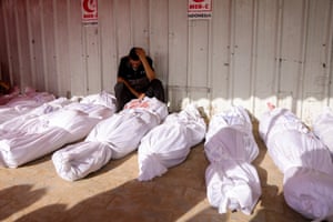 A Palestinian sits with his head in his hands among the wrapped-up bodies of people killed by Israeli strikes on Jabaliya