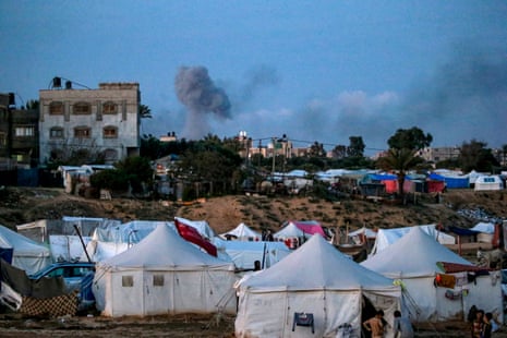A view of shelters used by Palestinian families who fled their homes in the northern Gaza Strip, while smoke rises in the background after an Israeli airstrikes in an area of Khan Younis on Wednesday evening.