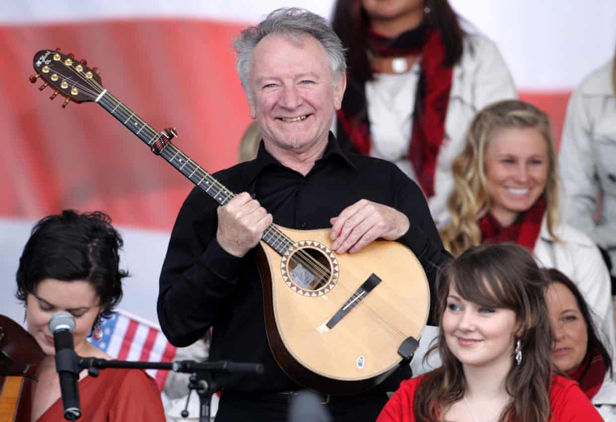 Musician Donal Lunny smiles before a crowd holding an stringed madolin-type instrument
