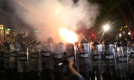 Rows of riot police confronting protesters at night