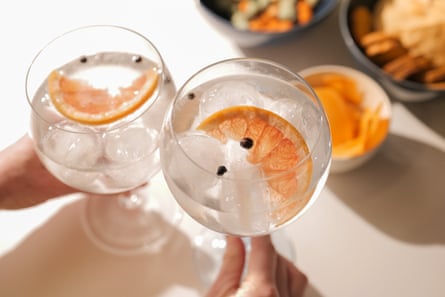 Two gin and tonic cocktails with juniper berries and a grapefruit slice in each glass, on a bar table with snacks