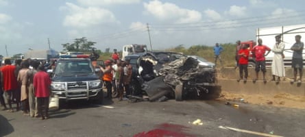 A badly damaged vehicle on the side of the road with a police car next to it and a large crown of people.