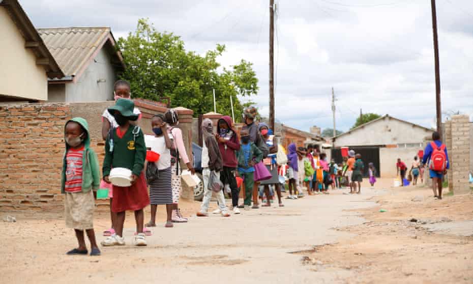 Children wait in a line to receive porridge in Chitungwiza, Zimbabwe, 3 December 2020