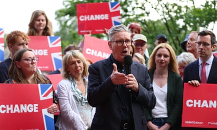 He stands speaking surrounded by people holding placards that read ‘change’