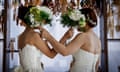 A lesbian couple in white gowns holding bouquets over their faces