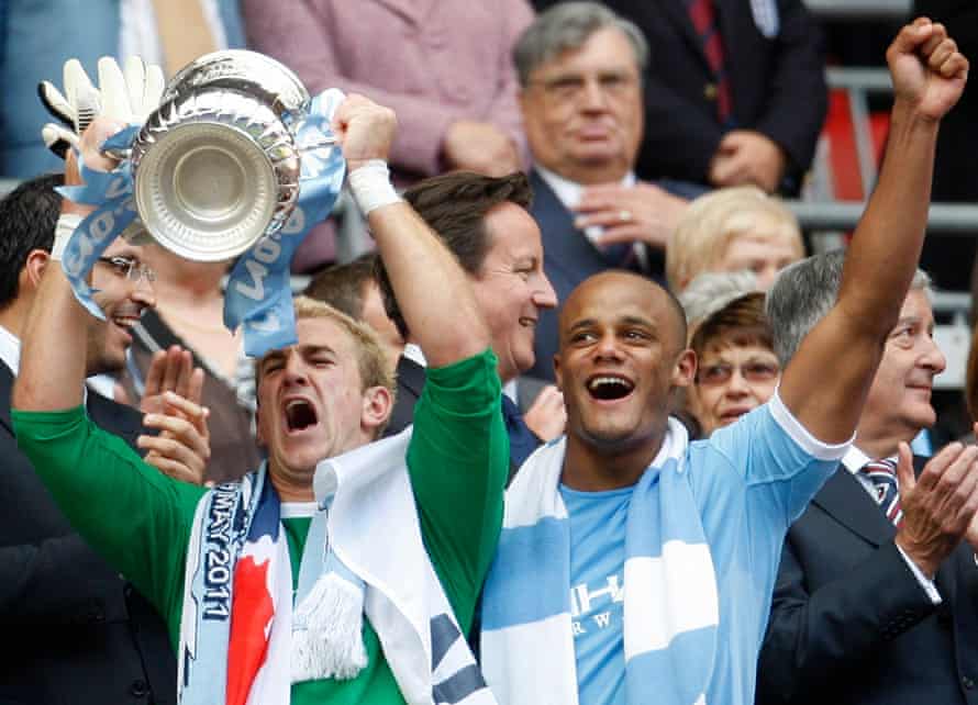 Manchester City’s Joe Hart (L) lifts the FA Cup as Vincent Kompany celebrates winning the FA Cup final against Stoke City, in May 2011