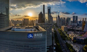 High-level view of skyscrapers in front of a sunset in Shanghai. A building bearing the Alipay logo is closest to the camera