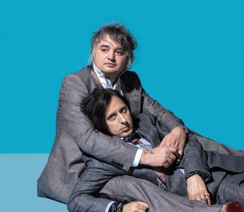 The Libertines' Pete Doherty and Carl Barât, sitting on the floor, the former with his arms around the latter, against a turquoise background