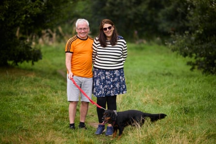 A middle-aged couple standing in a grassy field. The man has a dog on a lead.