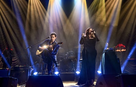 Mark Ronson plays guitar while Yebba sings into a microphone onstage under dramatic lighting