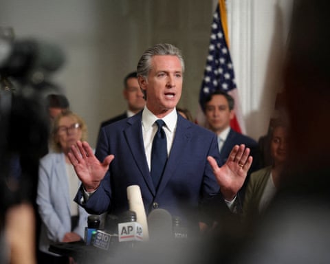 person wearing navy suit and tie speaks behind microphones while gesturing with hands