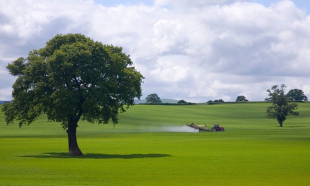 Farm tractor spraying insecticide on to green fields in England