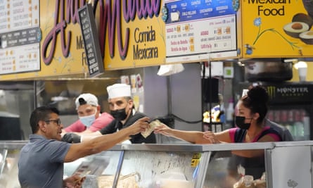 A man stretching over a counter to pick up food from a worker