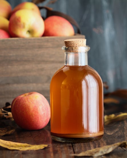 A glass jar of apple cider vinegar alongside an apple