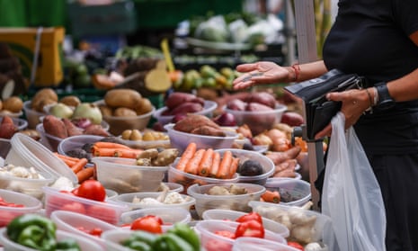A customer pays for fruit and vegetables at a grocery stall on Surrey Street Market in Croydon, UK.