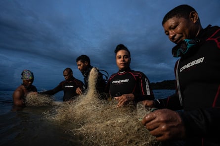 Five people in wetsuits hold a tangle of fishing nets