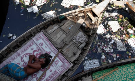 A man sleeps in his boat, anchored in the polluted waters of the Buriganga river in Dhaka, Bangladesh