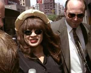 A woman wearing a hat and sunglasses walks with a man in a suit