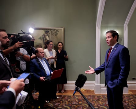 Marco Rubio gestures while speaking to reporters, who are holding cameras and microphones