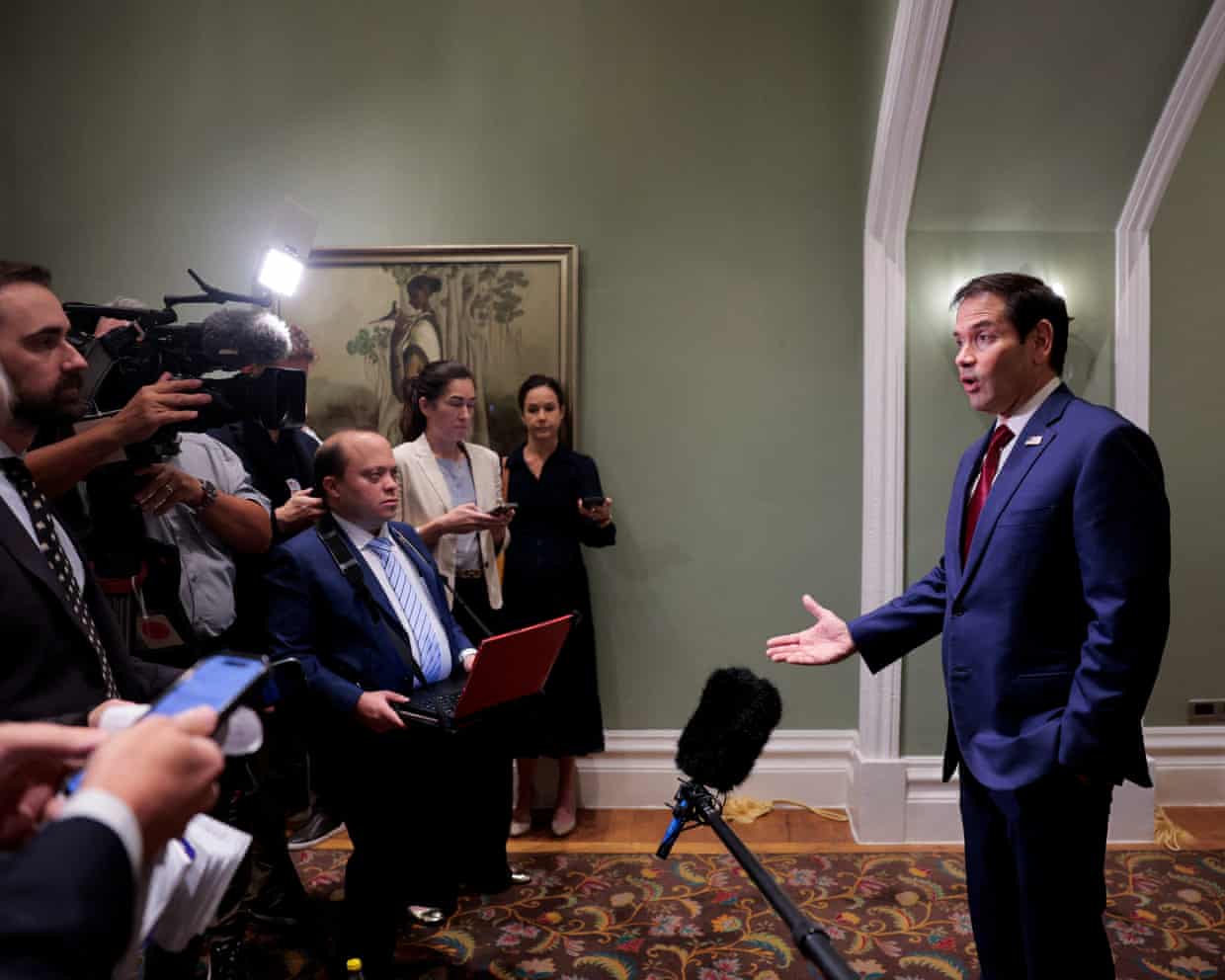 Marco Rubio gestures while speaking to reporters, who are holding cameras and microphones