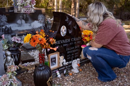 a woman crouches down before a grave site filled with flowers and figurines