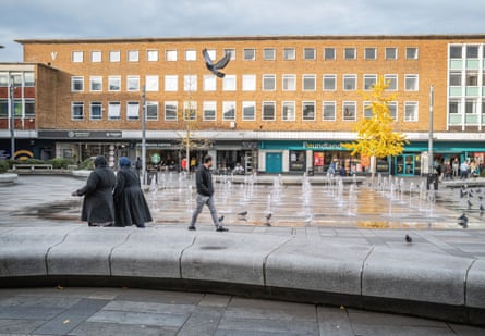 People walk past fountains in a square in the centre of Crawley