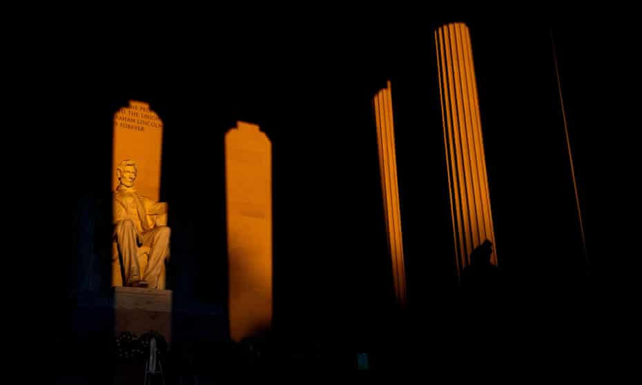 The statue of Abraham Lincoln is illuminated at sunrise as a visitor walks through the Lincoln Memorial in Washington.