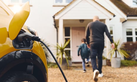 Electric car charging on driveway outside house as a man and a child head towards the front door