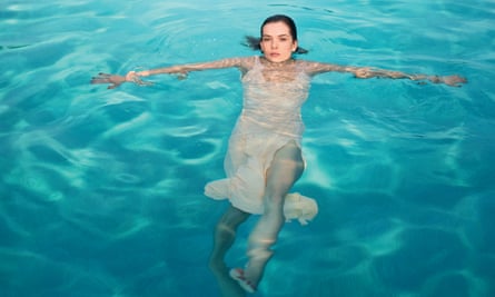 A model in a swimming pool wearing a dress looks towards the camera