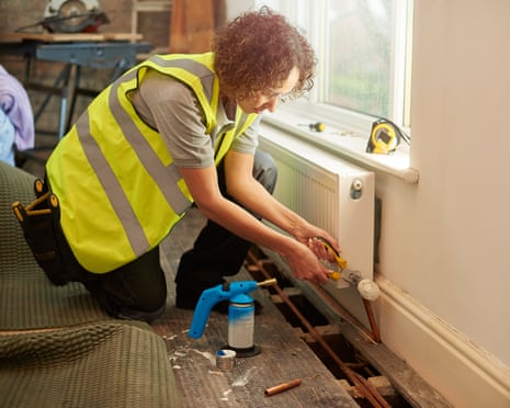 female plumber on site<br>a mid adult female plumber is installing a new radiator into a property undergoing refurbishment. The floorboards are raised with new paperwork shown , and she is tightening the valve on the new radiator. She is wearing work trousers , and tool belt . In the background more work tools can be seen as is an exposed brick wall .