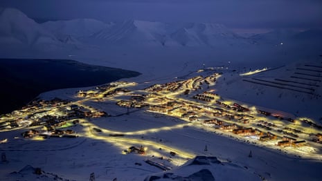 An illuminated village spread across a snowy valley at night, surrounded by dark mountains