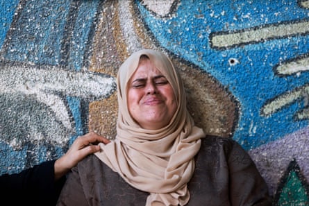 A woman in a hijab looking anguished with her eyes closed, a comforting hand laid on her shoulder
